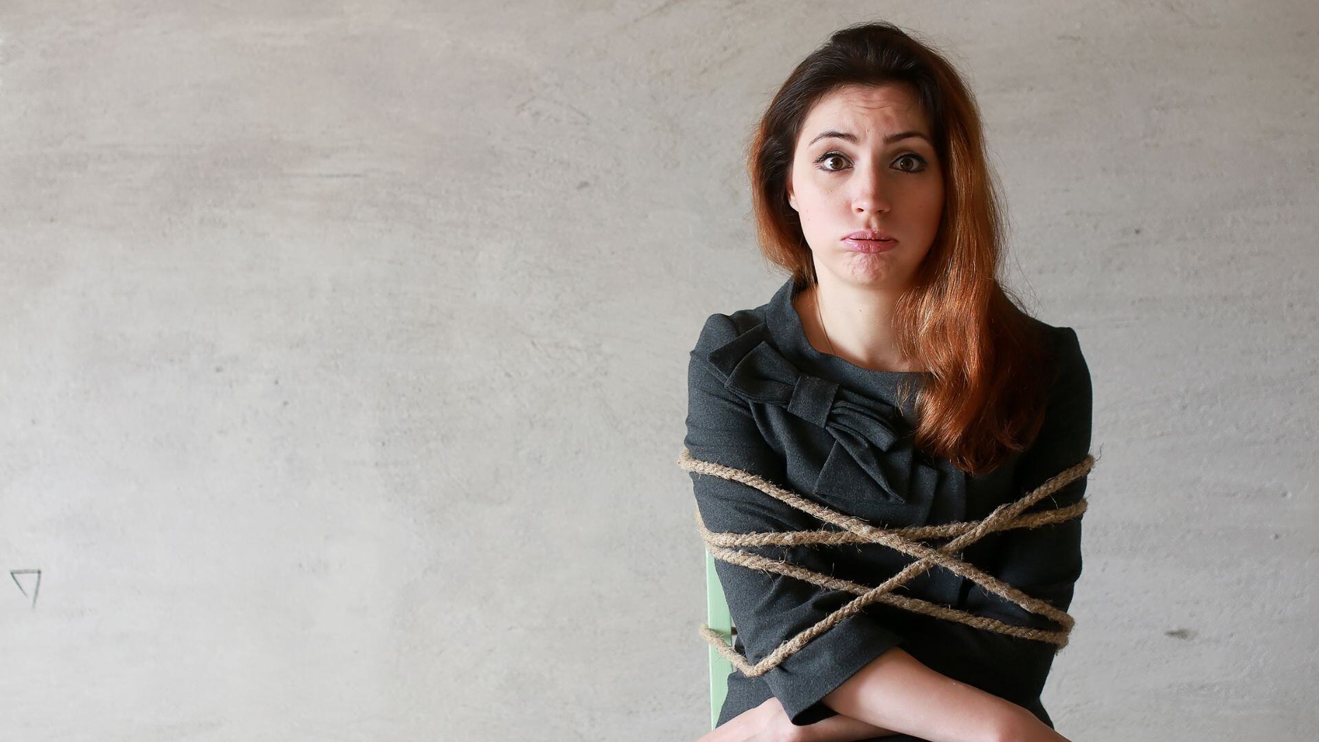 A businesswoman sits in a chair tied up with rope.